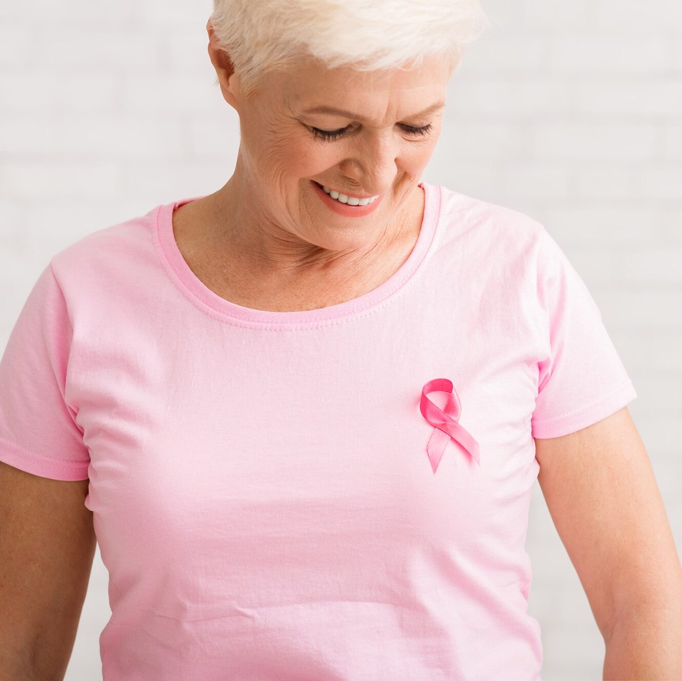 Elderly Woman Looking At Pink Cancer Ribbon On T-Shirt, Indoor